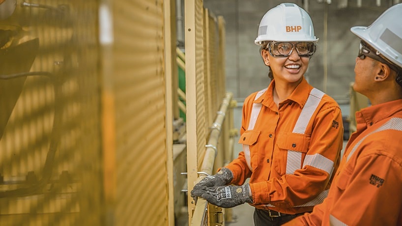 Three women in BHP orange shirt and hat uniform standing with Jansen sit in the background of a green field