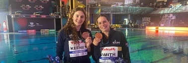 two women at a swimming pool in tracksuits showing medals around neck